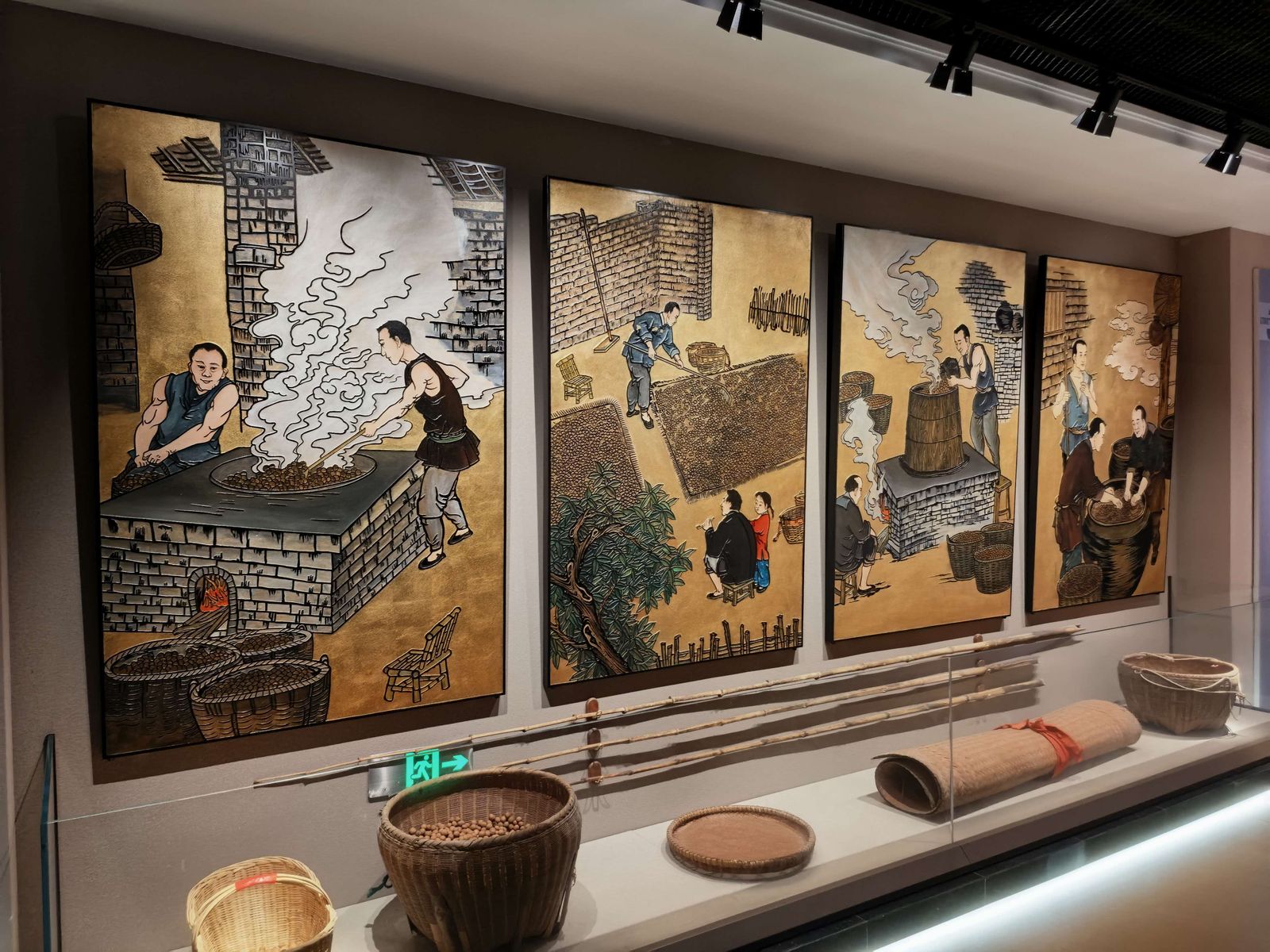 展墙上是四联工笔壁画，再现炒制、摊晒、蒸煮、筛分的旧工序；墙下陈列着扁担与竹匾。