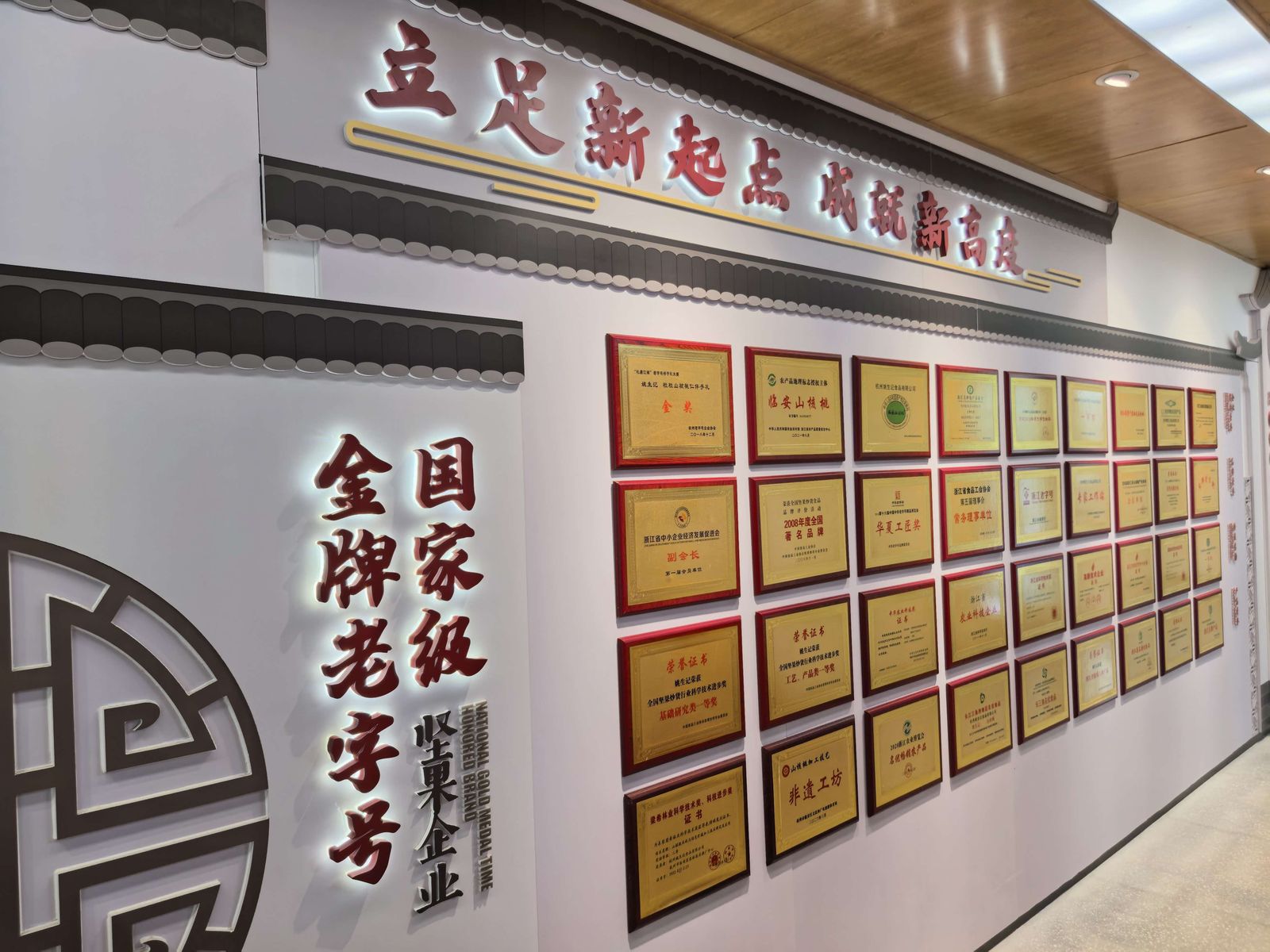 荣誉墙上方悬着「立足新起点 成就新高度」，左侧写着「国家级 金牌老字号 坚果企业」。